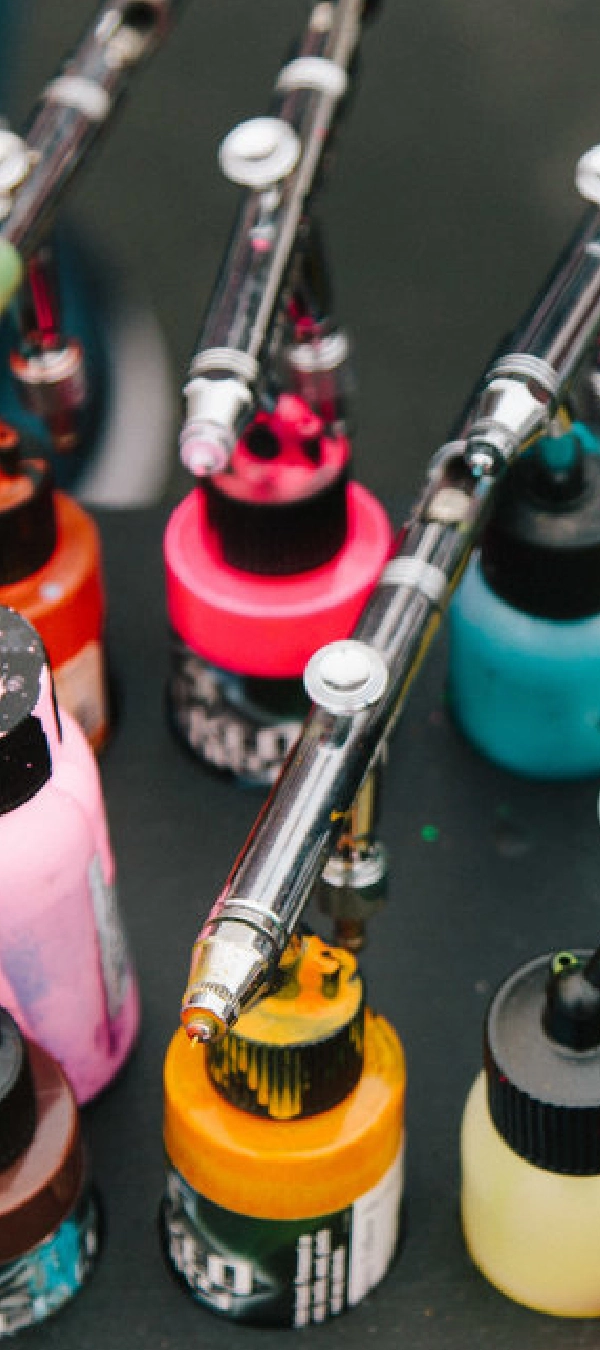 Airbrush guns rest on colorful ink bottles, showcasing a vibrant setup reminiscent of an airbrush artist's colorful palette for events.
