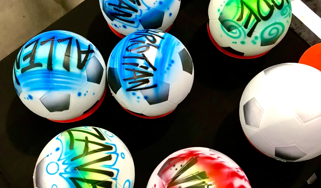 Soccer balls featuring vibrant airbrush art designs and names are elegantly arranged on a dark surface.